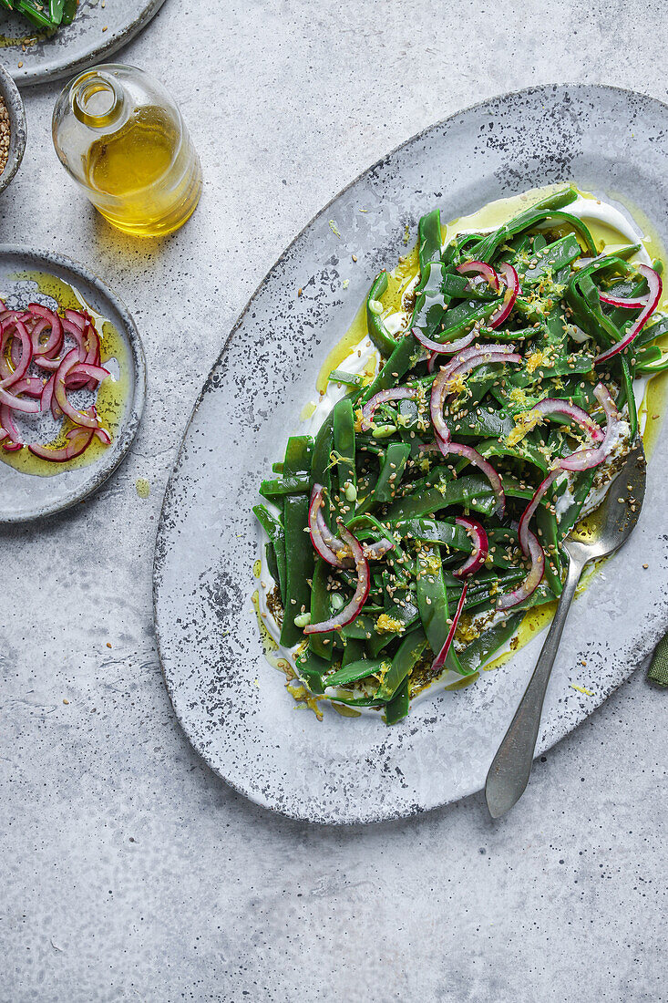 Draufsicht auf einen appetitlichen vegetarischen Salat mit grünen Kräutern und Zwiebelscheiben, der auf einem Teller mit Öl serviert und mit Zitronenschalen garniert wird