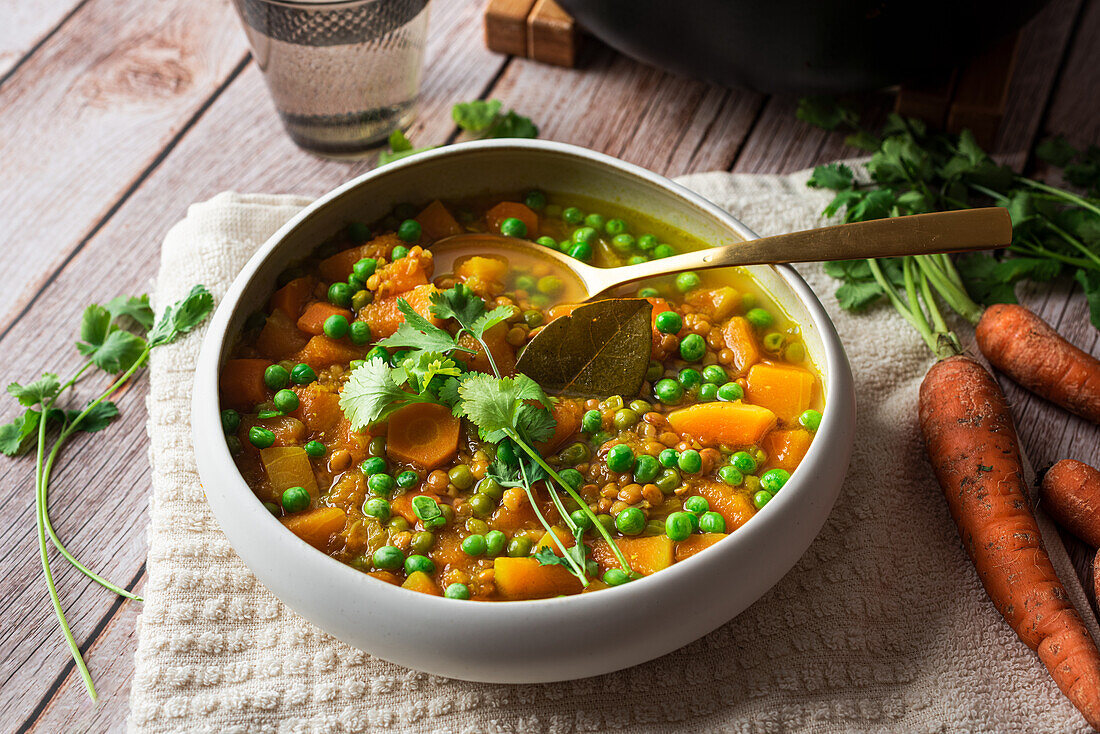 Von oben appetitliche frisch gekochte Suppe mit Karotten und grünen Erbsen, serviert in einer weißen Keramikschüssel auf einem Holztisch, dekoriert mit einem Petersilienzweig