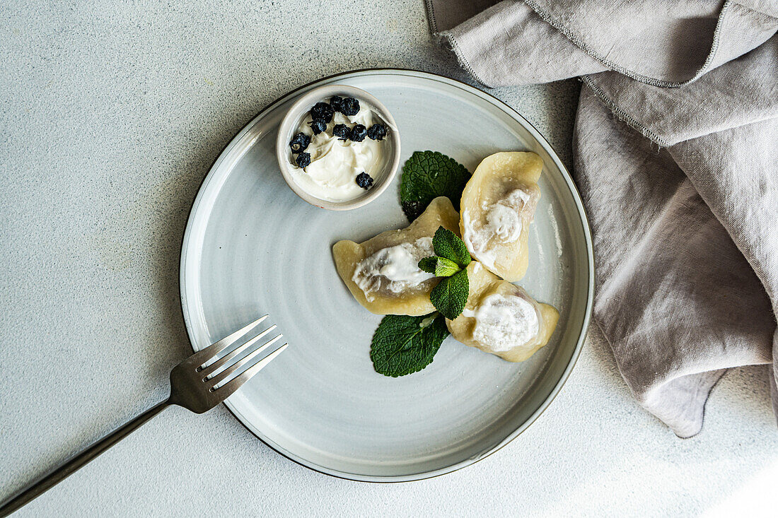 Top view of a tasty traditional Ukrainian dumplings with cherry and sour cream with mint