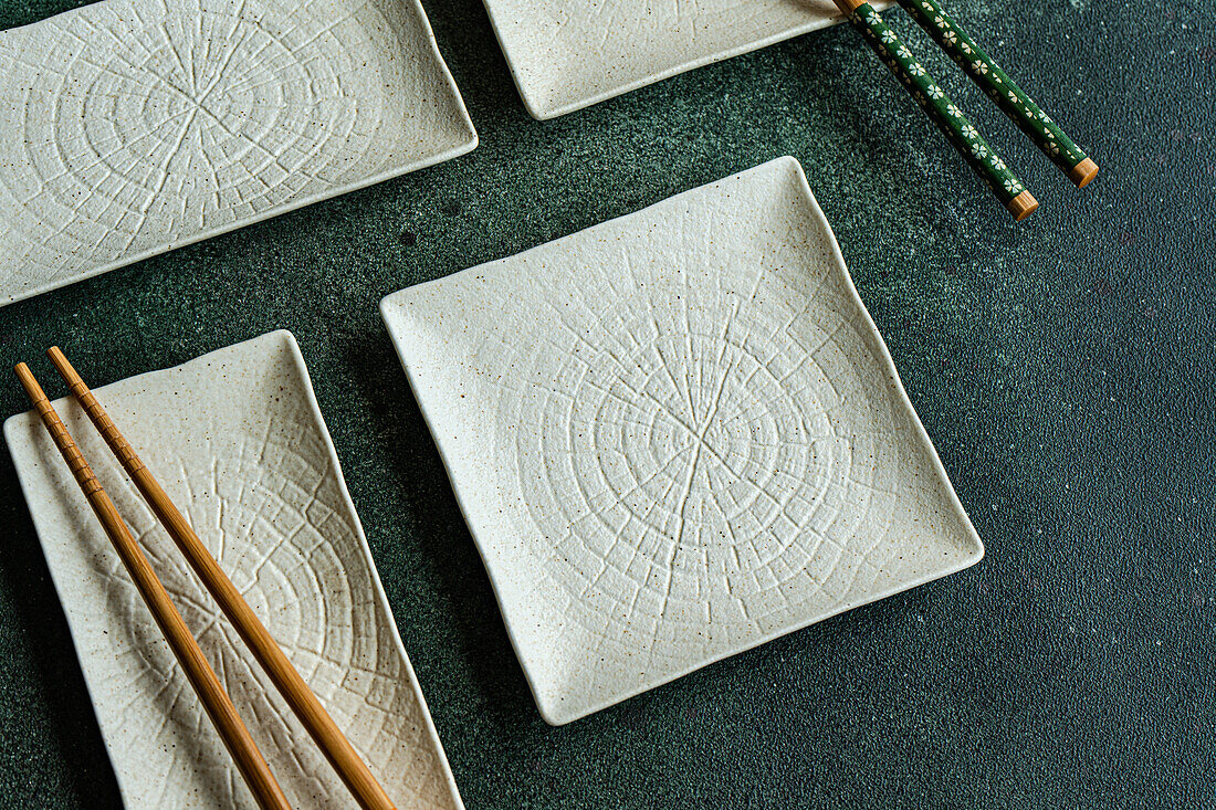 From above of set of white ceramic plates of placed on concrete black table with chopsticks in Asian restaurant