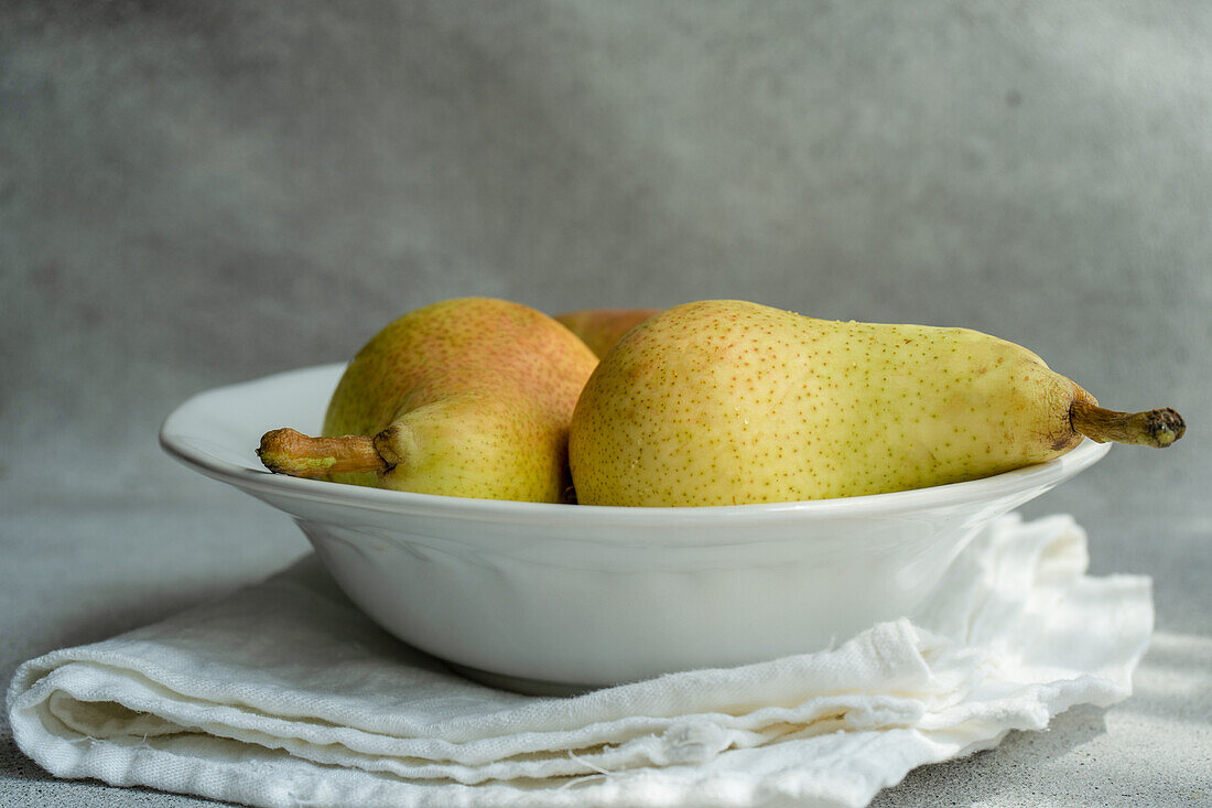White marble bowl with fresh juicy pears placed on a concrete table