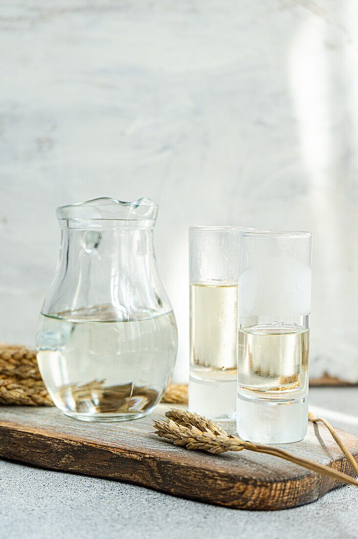 Traditionelles ukrainisches alkoholisches Getränk aus Weizen, bekannt als Gorilka, serviert in einem transparenten Glas und Gläsern auf einem Schneidebrett vor einem unscharfen Hintergrund