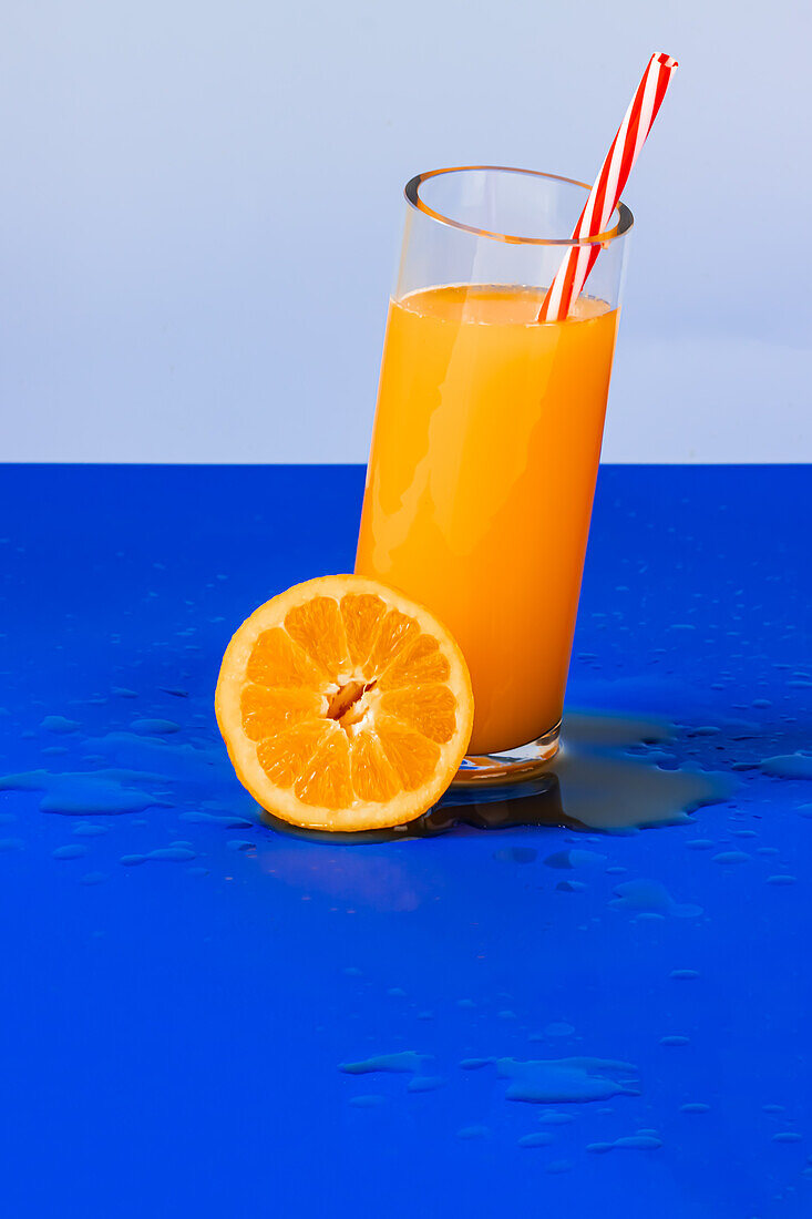 Nahaufnahme eines Glases mit Orangensaft-Cocktail und einer frischen Orangenscheibe auf blauem Hintergrund