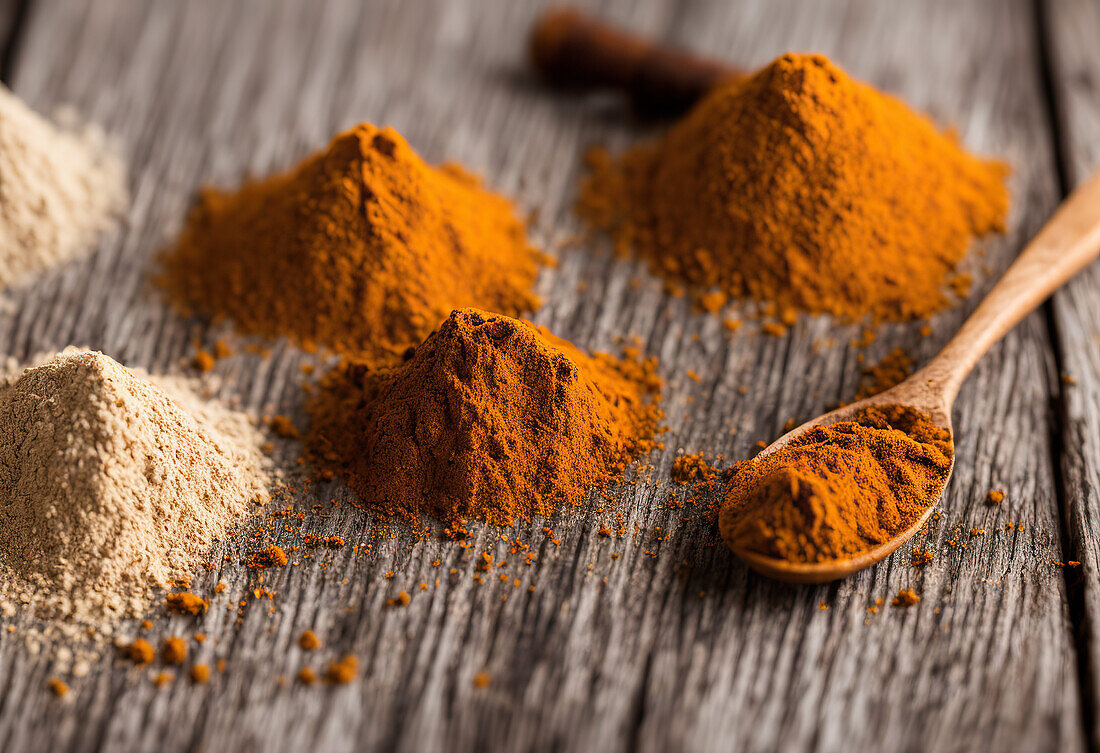 High angle of heap of colored powdered spices and wooden spoon placed on wooden table as sample