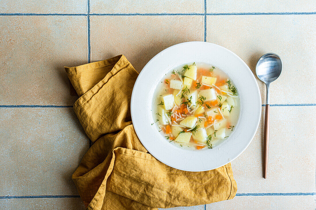 Von oben servierte gesunde Suppe mit Karotten und Kartoffeln auf gefliestem Keramikhintergrund
