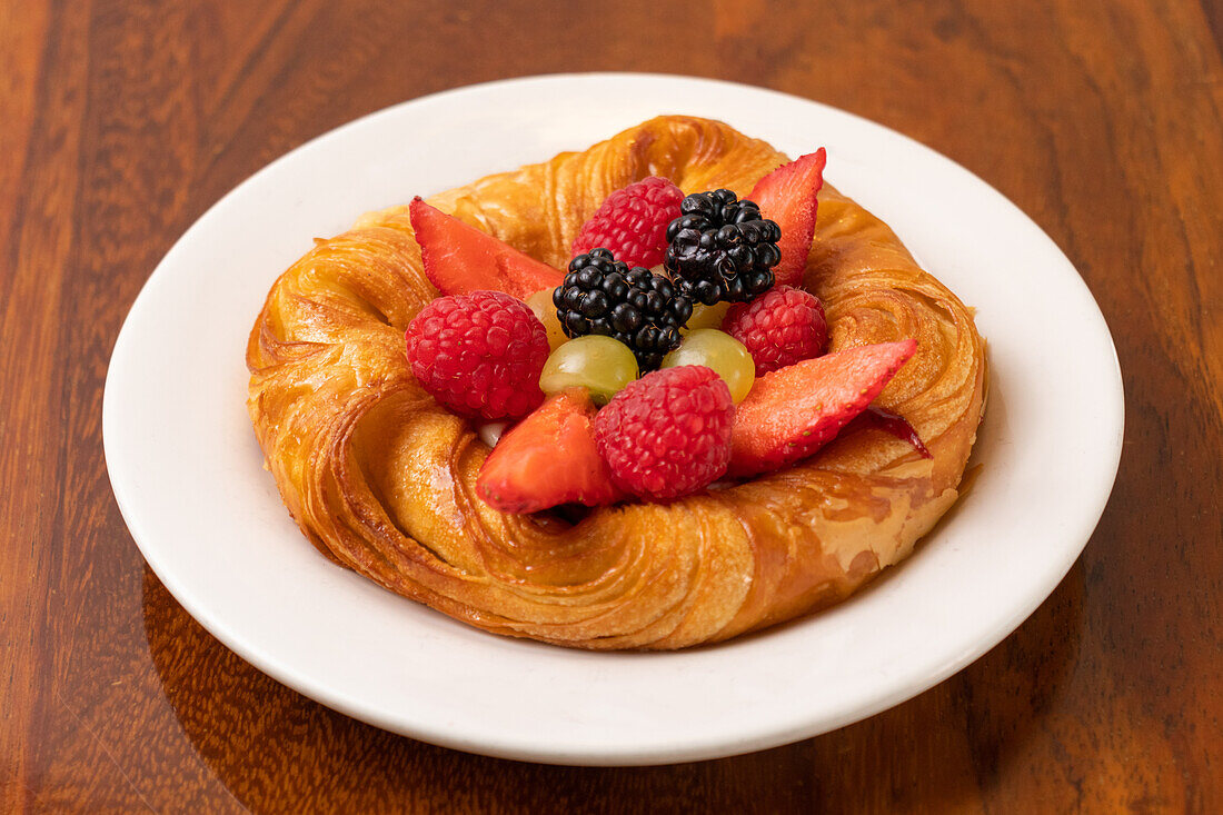 Draufsicht auf appetitlich gebackene Croissants mit Erdbeeren und Brombeeren mit Trauben auf weißem Teller über Holztisch serviert