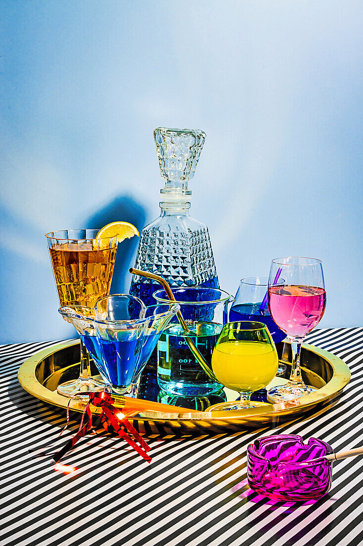 Verschiedene Cocktails, darunter eine blaue Margarita Long Island Eistee Wein Daiquiri in attraktiven Gläsern und Gläsern auf einem Teller auf gestreiftem Tuch vor blauem Hintergrund