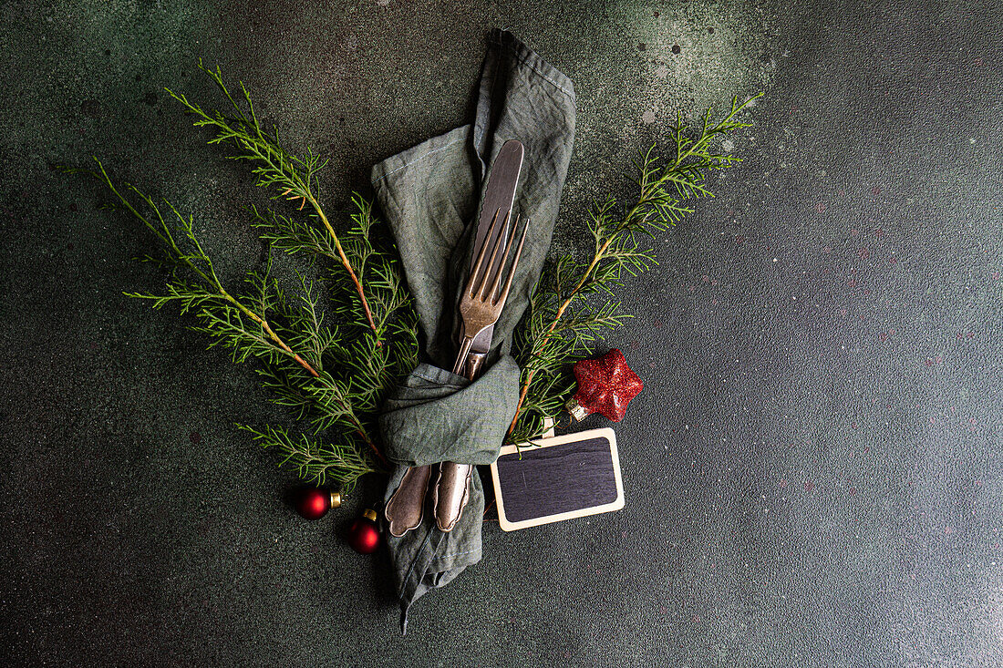 Top view of Christmas composition of fork and knife wrapped in handkerchief near green fir sprigs placed on gray background