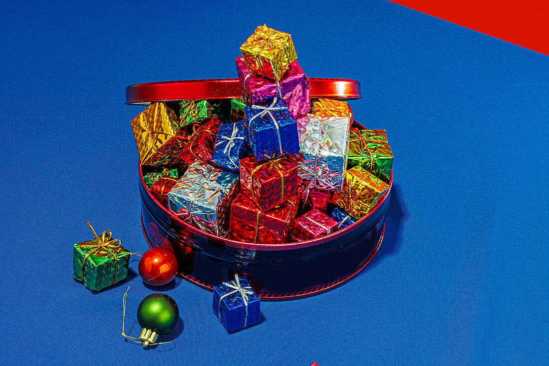 Draufsicht auf einen roten Behälter voller bunt verpackter Weihnachtsgeschenke auf einer blauen Fläche mit rotem und blauem Hintergrund