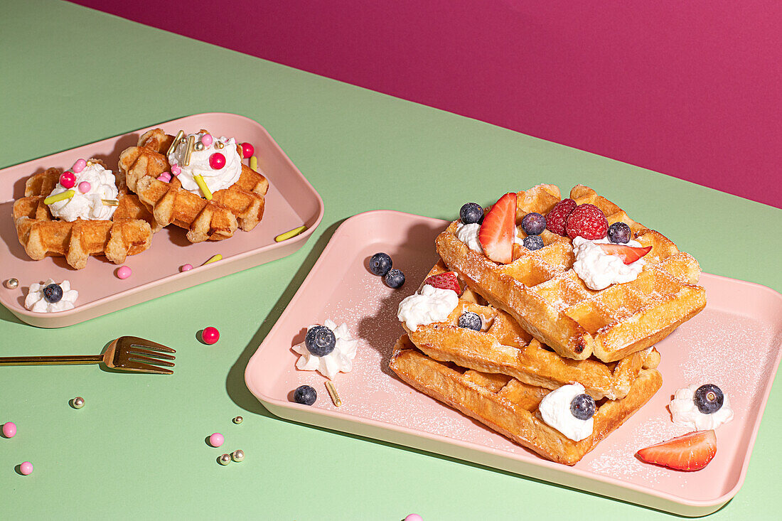 From above tasty sweet waffles topped with berries fruits sauce and cream served on pink tray on colorful table background in light kitchen