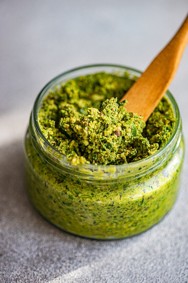 Von oben: Frische grüne Pesto-Sauce und Holzlöffel auf dem Tisch bei der Vorbereitung einer gesunden Mahlzeit zu Hause