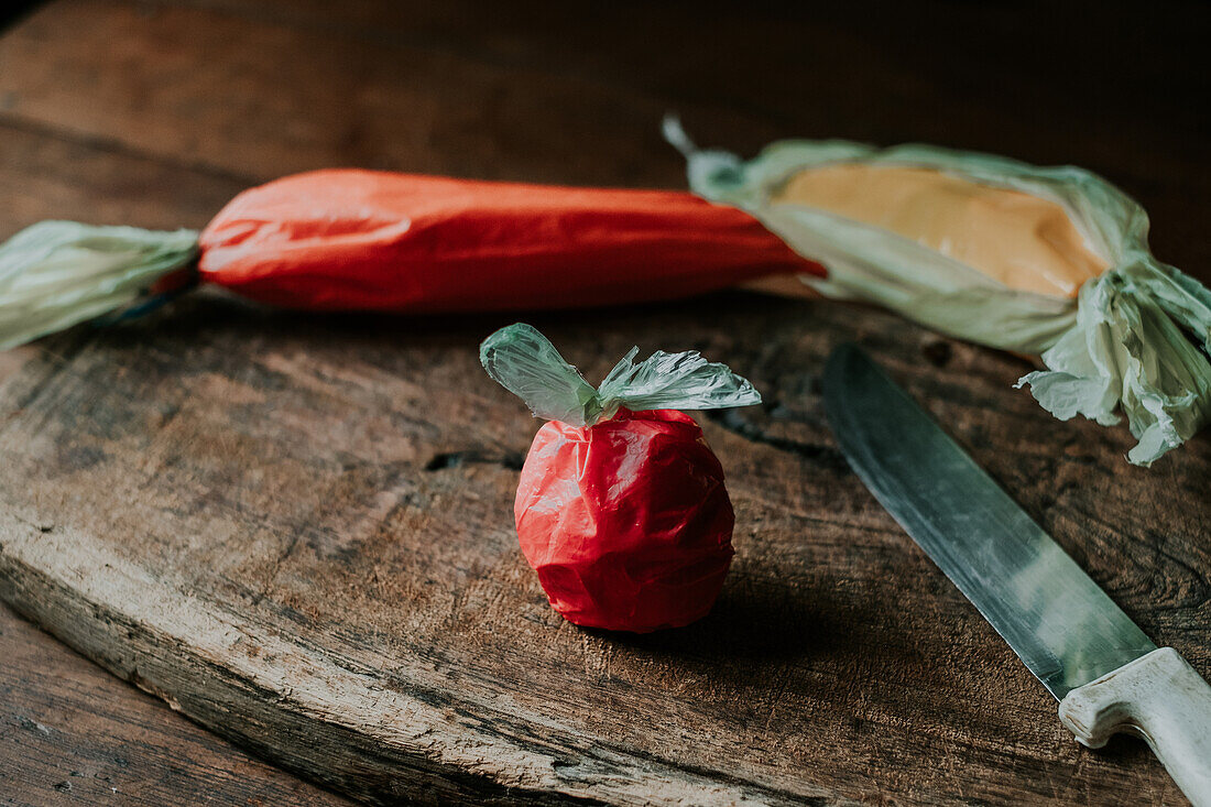 Plastiktüten in Form einer Tomate, Karotte und Paprika neben einem Messer auf einer gealterten Holzoberfläche