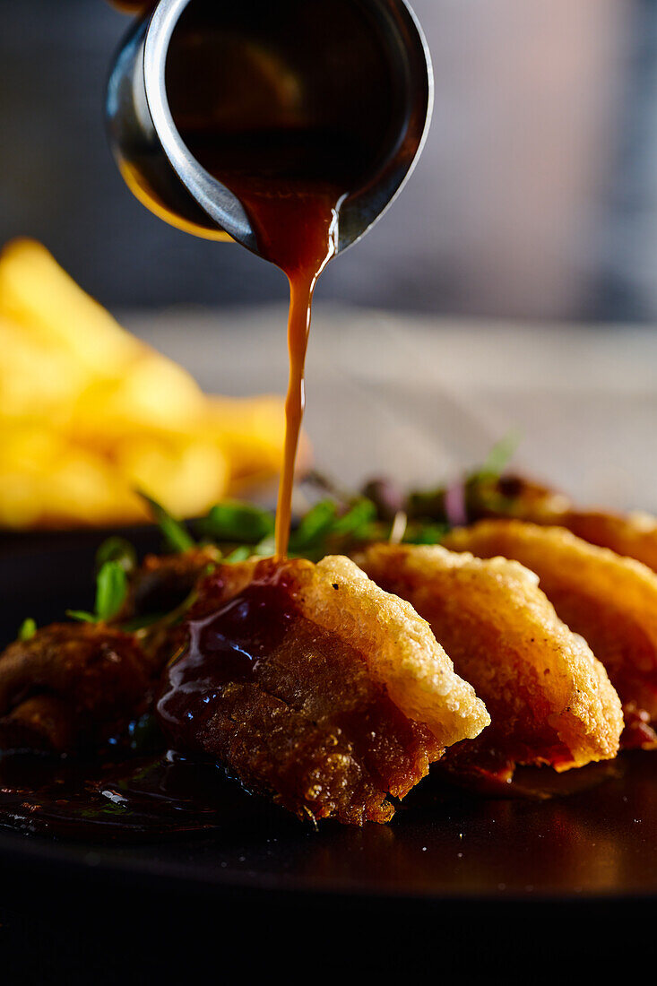 Cook preparing traditional Ecuadorian dish pouring sauce on appetizing fried breaded meat served on plate against blurred background