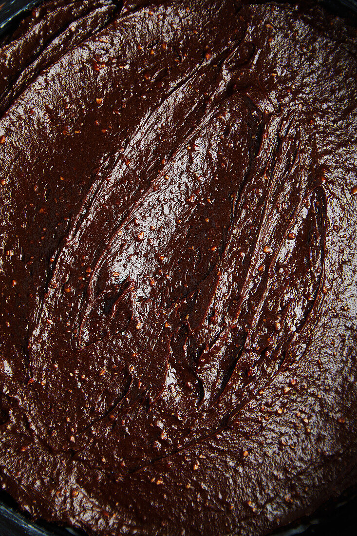 Nahaufnahme von glänzender Oberfläche von Teig für Schokoladenkuchen in Backform in weichem Licht