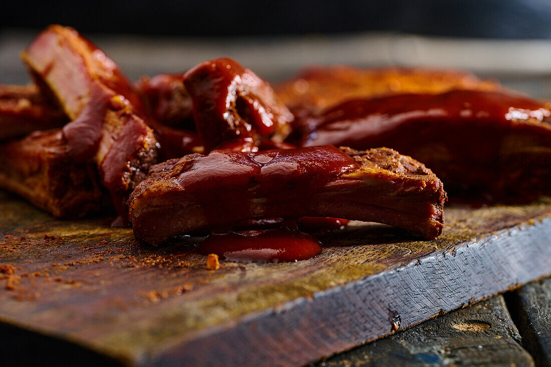 Front view of appetizing grilled pork ribs with barbecue served on wooden board in kitchen against blurred background