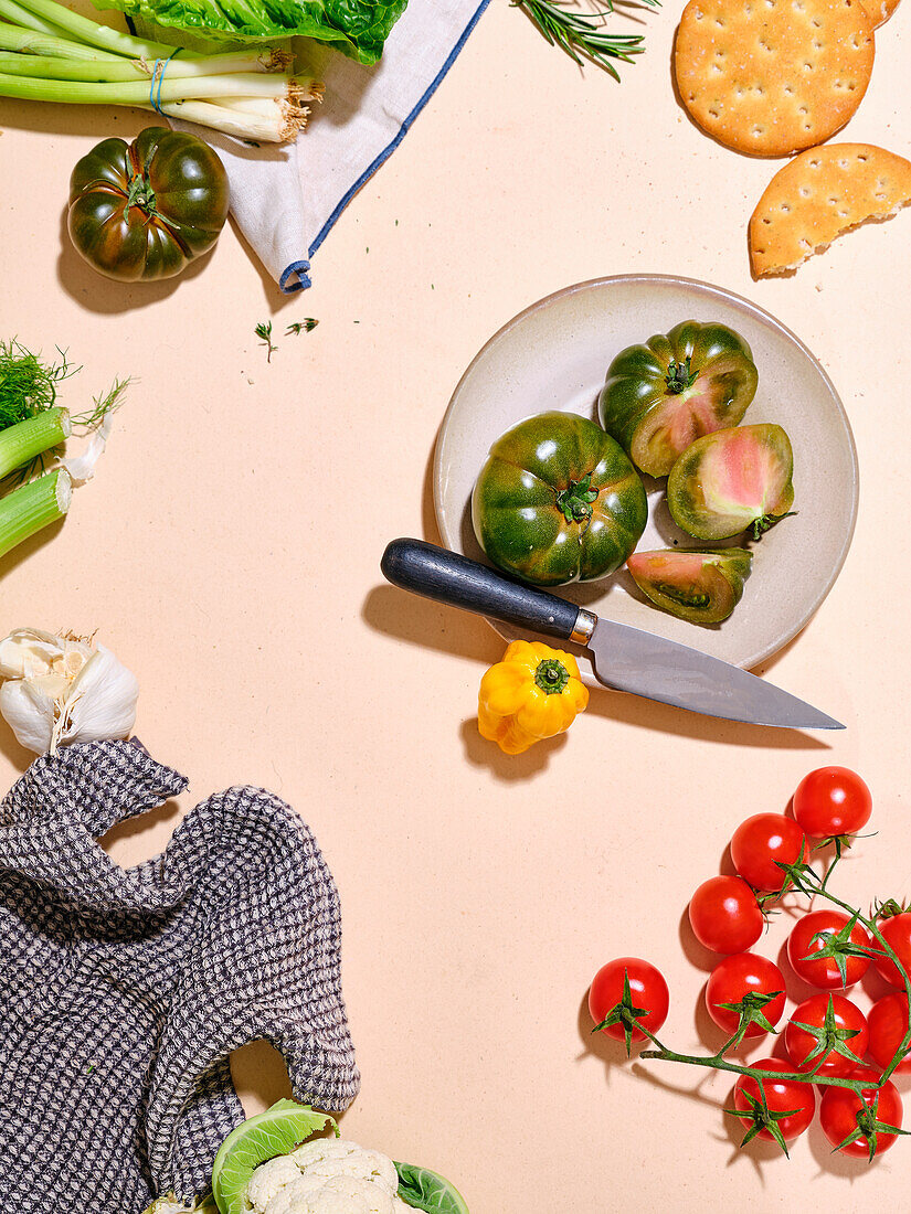 Grüne Tomaten mit anderem Gemüse wie Bok Choy in hellem Sonnenlicht flachgelegter Teller mit Messer mit Kopierraum auf beigem Hintergrund