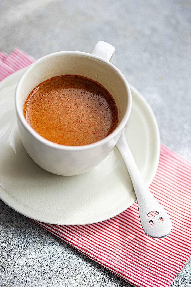 High angle of crop cup of spicy espresso with spoon placed on napkin against gray table