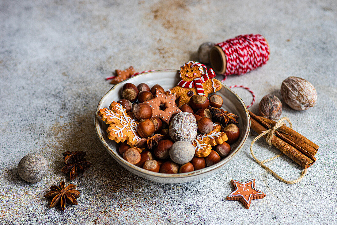 From above of plate of heap of chestnuts with tasty Christmas cookies placed on table near spool of red thread