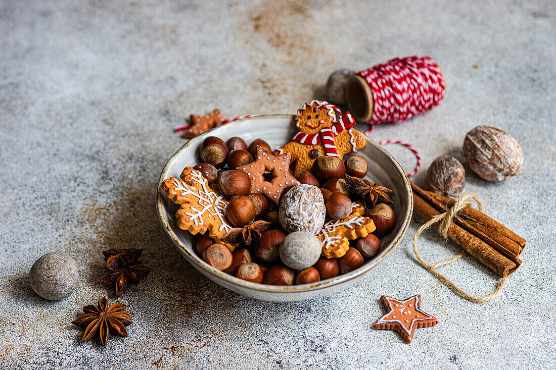 Von oben auf einen Teller mit einem Haufen Kastanien und leckeren Weihnachtsplätzchen, die auf einem Tisch neben einer Spule mit rotem Faden liegen