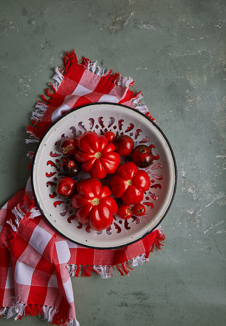 Top view of fresh red cherry and beef tomatoes placed on plate over checkered cloth on gray table background