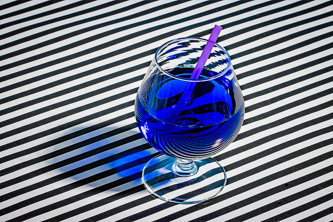 High angle of blue cocktail glass garnished slice straw while served on stripes cloth surface