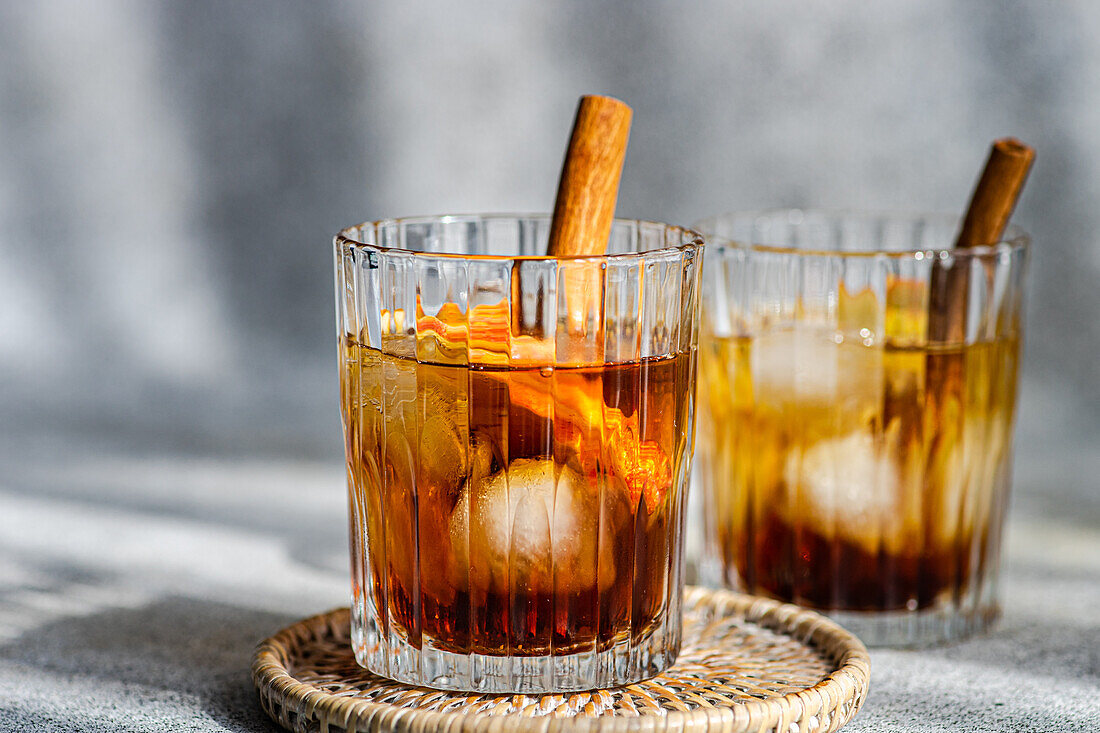 Fresh apple cider cocktails garnished with cinnamon sticks, star anise, and apple slices in a crystal glass filled with ice cubes on a textured background