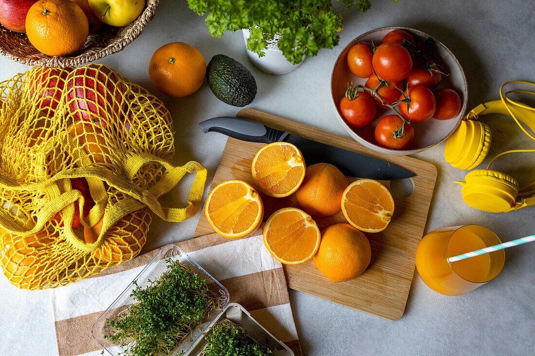 Hoher Blickwinkel auf gesunde geschnittene Orangen mit verschiedenen Gemüsen und Früchten in einem Netzbeutel mit Kopfhörern auf dem Tisch zu Hause