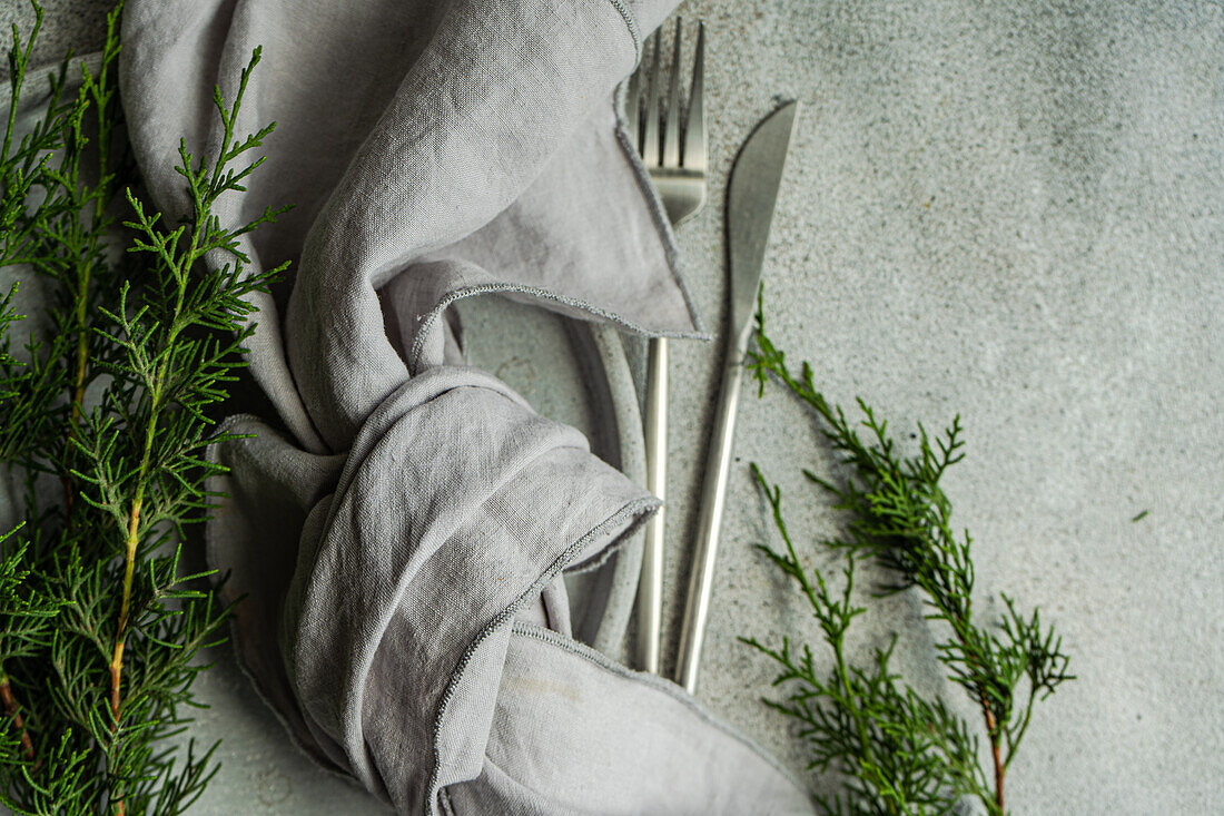 Draufsicht auf eine weihnachtliche Komposition aus Gabel und Messer zusammen in einem Taschentuch neben grünen Tannenzweigen auf grauem Hintergrund