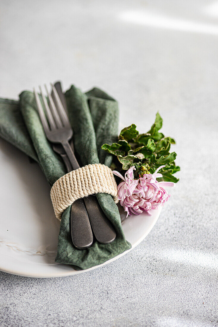 Ein raffinierter Teller mit Silberbesteck in eine grüne Serviette eingewickelt, mit frischen Blumen akzentuiert