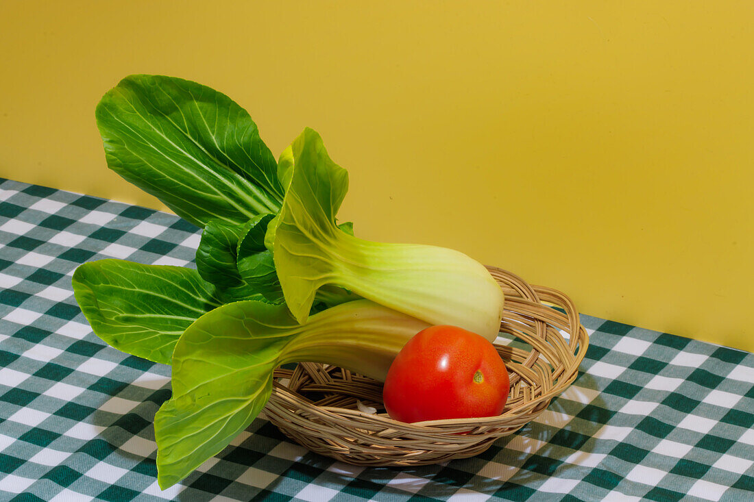 Frischer grüner Bok Choy-Kohl und rote, reife, saftige Tomaten auf einem karierten Tischtuch vor gelbem Hintergrund