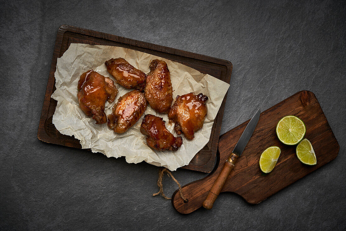 From above of appetizing grilled marinated chicken wings with ginger vinegar placed on plate with sauce and served with onions on wooden cutting board with knife on gray hard surface