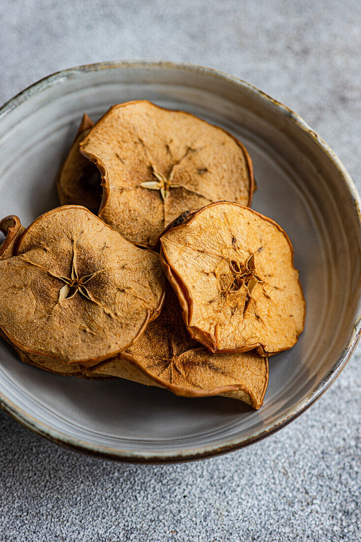 High angle of slices of dried apples served in ceramic bowl against blurred gray background