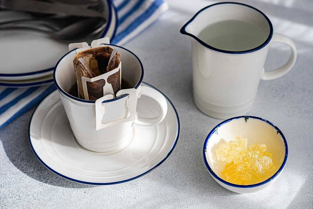 Ein gemütlicher Morgenkaffee mit einem Tropfkaffeefilter über einer Keramiktasse, neben einer Kanne Milch und einer Schale mit Rohzucker