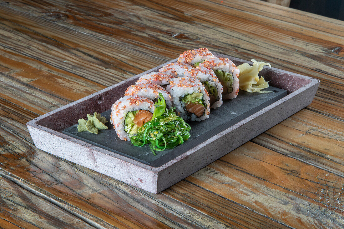 Nahaufnahme einer servierten Reihe von Avocado-Thunfisch-Uramaki-Sushi-Rollen mit Wakame-Salat auf einem Betonteller