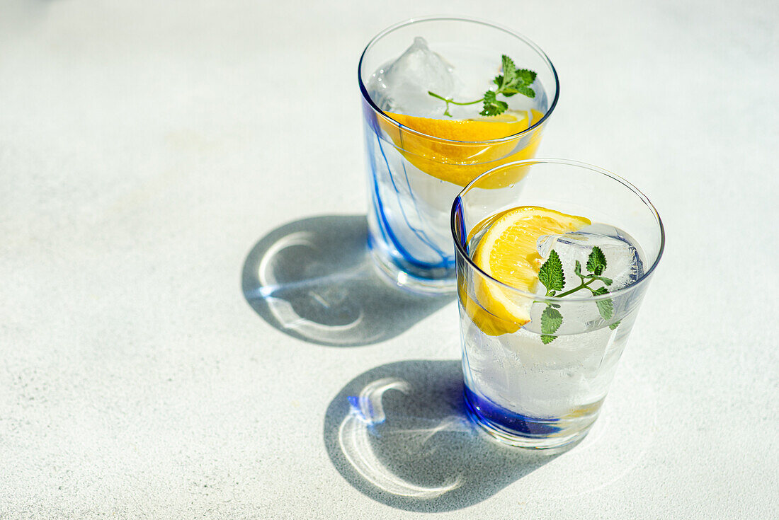 High angle of Summer cocktails with lemon vodka, slices of lemon and wild mint leaves served with ice placed on white table