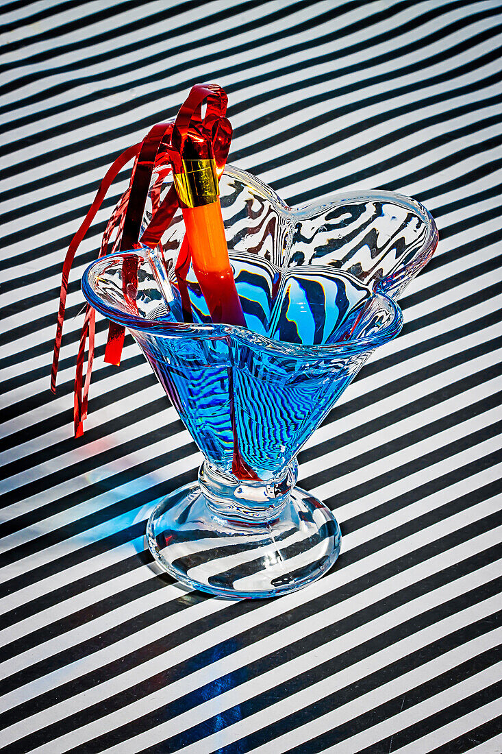 Hoher Winkel eines blauen Cocktailglases, garniert mit einem Strohhalm, serviert auf einer gestreiften Stoffoberfläche