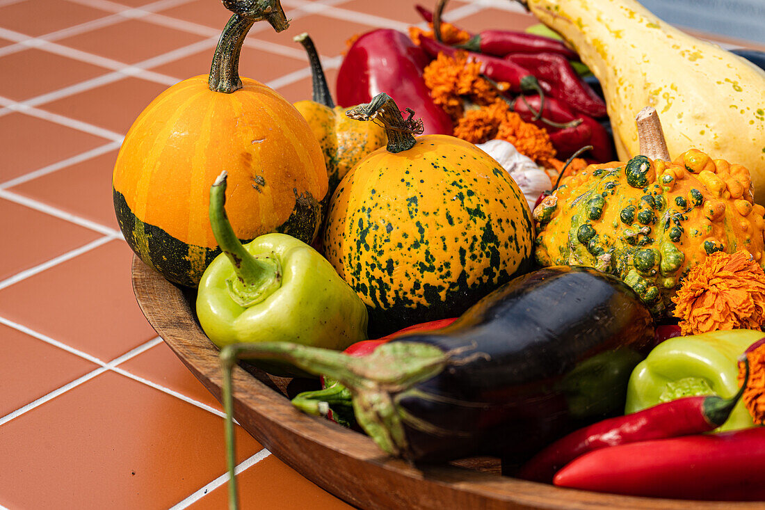 Pumpkins, eggplant and peppers in a big wooden bowl on a terracotta floor.
