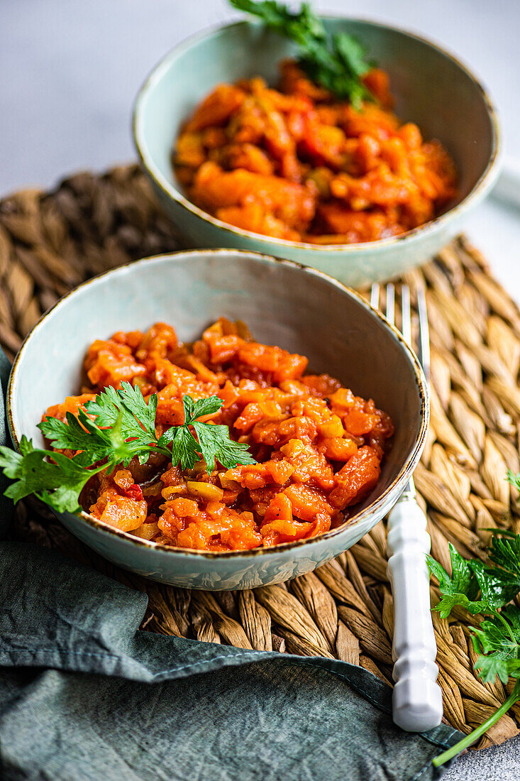 Gemüseeintopf aus Kartoffeln, Karotten, Paprika und Tomaten, serviert mit Petersilienblättern in einer Schüssel auf einem Betontisch (von oben)