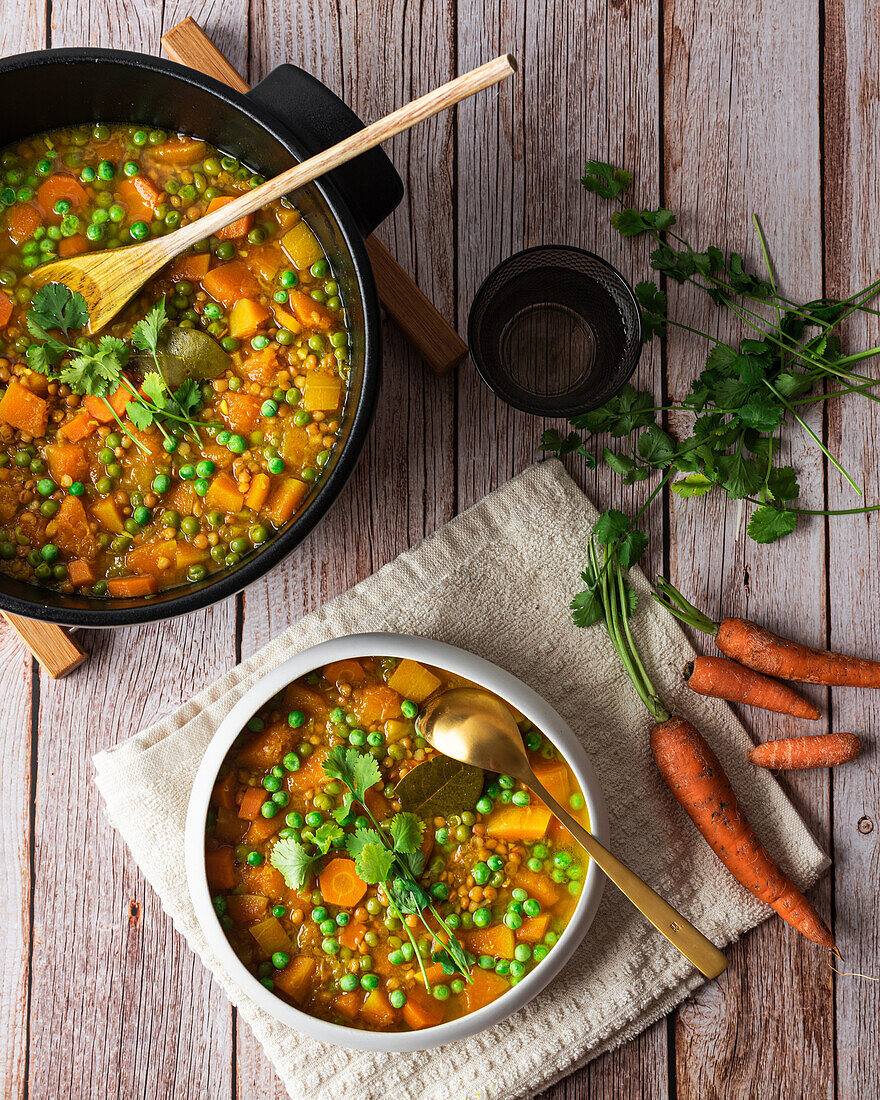 Top view of appetizing fresh cooked soup with carrot and green peas served in white ceramic bowl placed on wooden table and decorated with parsley branch