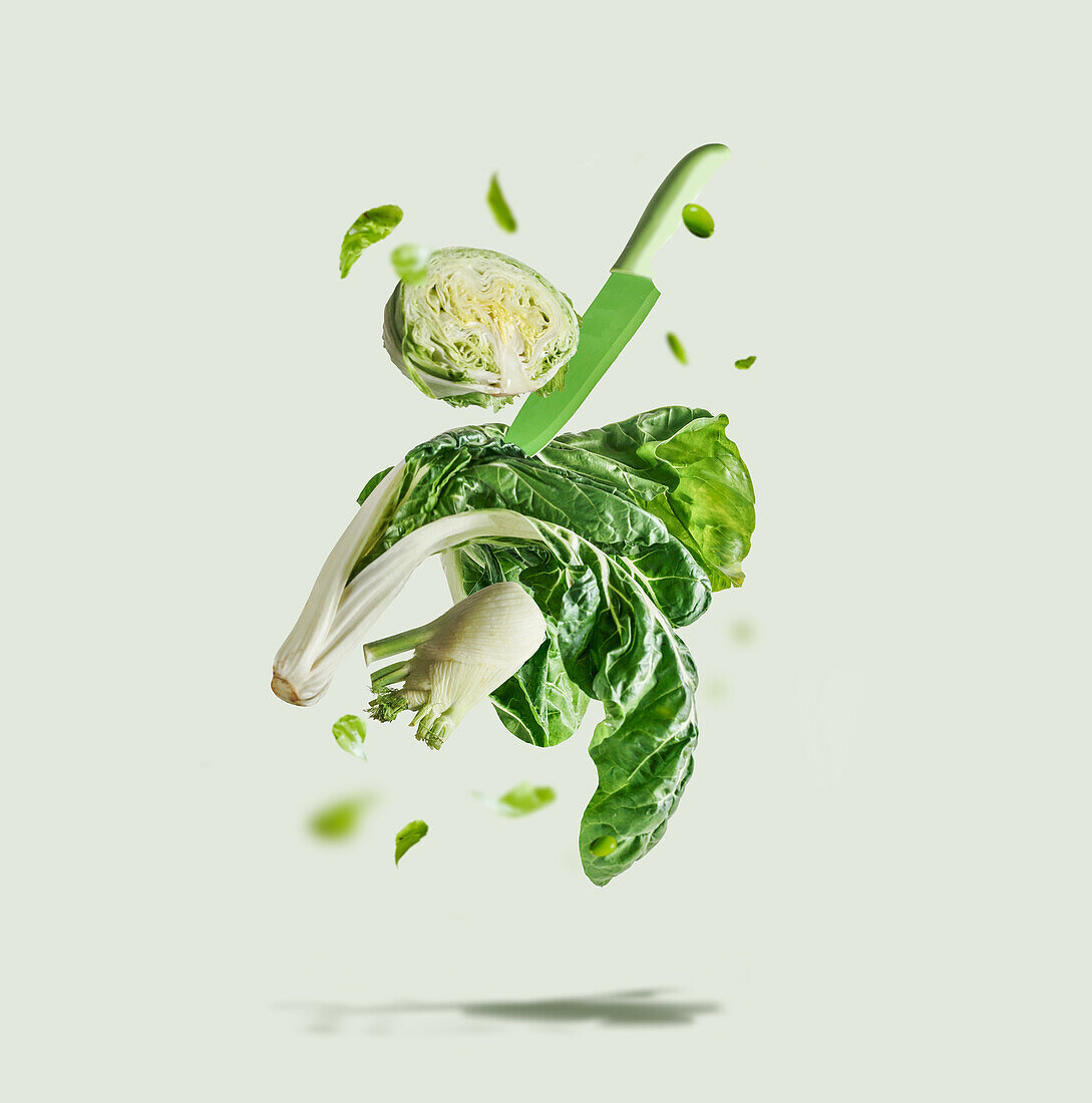 Fliegende grüne Gemüseauswahl mit Messer vor hellem Hintergrund. Zutaten für gesundes Essen: Salat, Fenchel, Bok Choy und Edamame, die in der Luft schweben. Vorderansicht