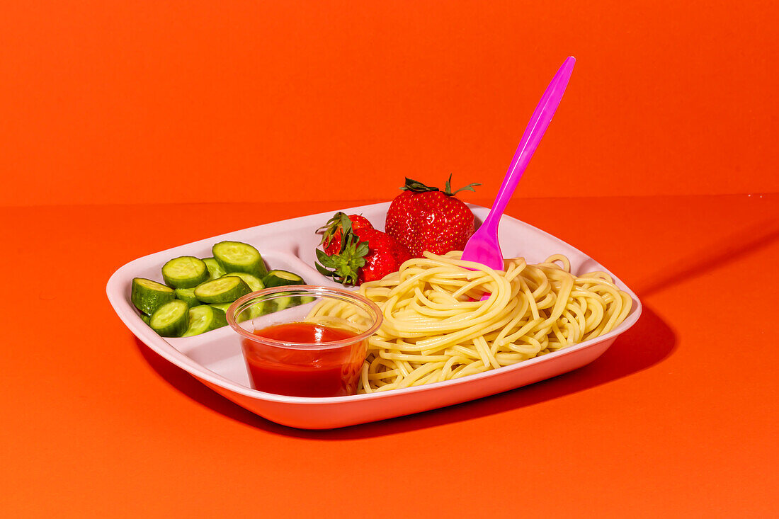 Front view composition of spaghetti with fork tomato sauce cucumber slices and yummy fresh strawberries served for school lunch on red top table