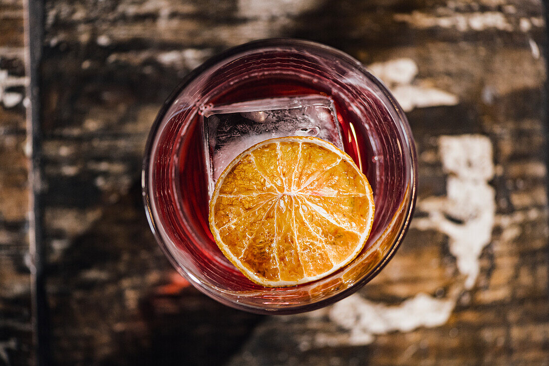 Draufsicht auf einen appetitanregenden, erfrischenden alkoholischen Negroni-Cocktail mit Orangenscheibe und Eiswürfel im Glas auf einem Tisch in einer Bar