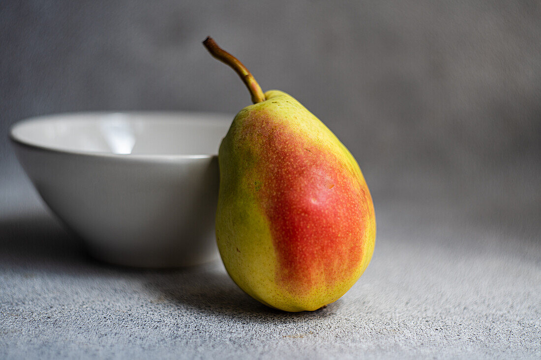 Front view of ripe organic pear fruit next to a bowl on gray blurred background