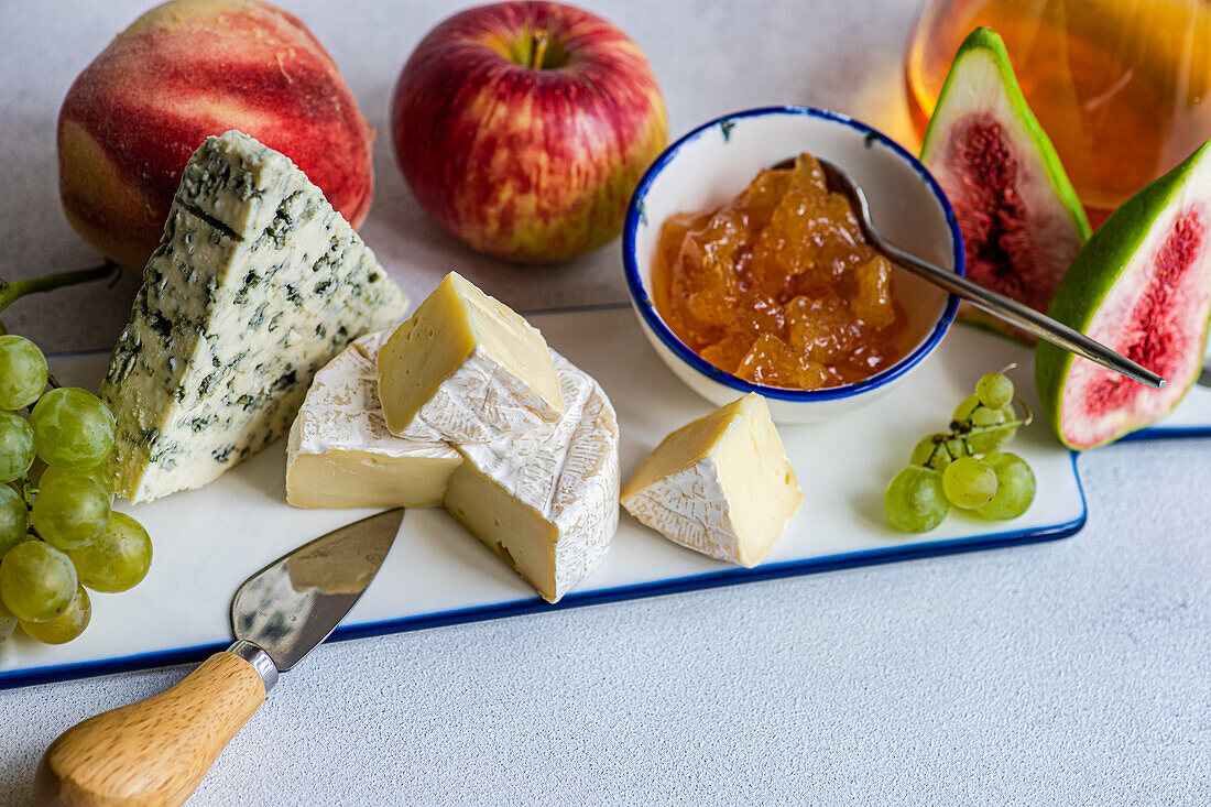 Von oben verschiedene leckere Snacks mit verschiedenen Käsesorten und Süßigkeiten auf einem Keramikteller mit Trauben, Äpfeln und Feigen auf dem Tisch serviert
