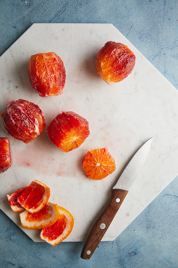 Top view of appetizing juicy whole bloody oranges placed on cutting board near knife and peel on table