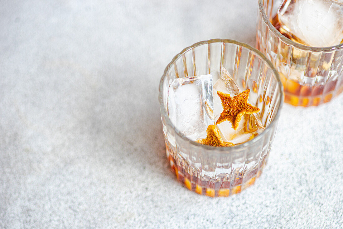 High angle of glasses of whiskey with ice and orange peel placed on gray background