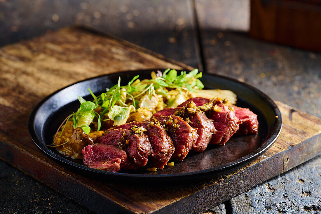 High angle of appetizing traditional Ecuadorian dish made of roasted meat with sauce herbs and vegetables served on black plate on cutting board