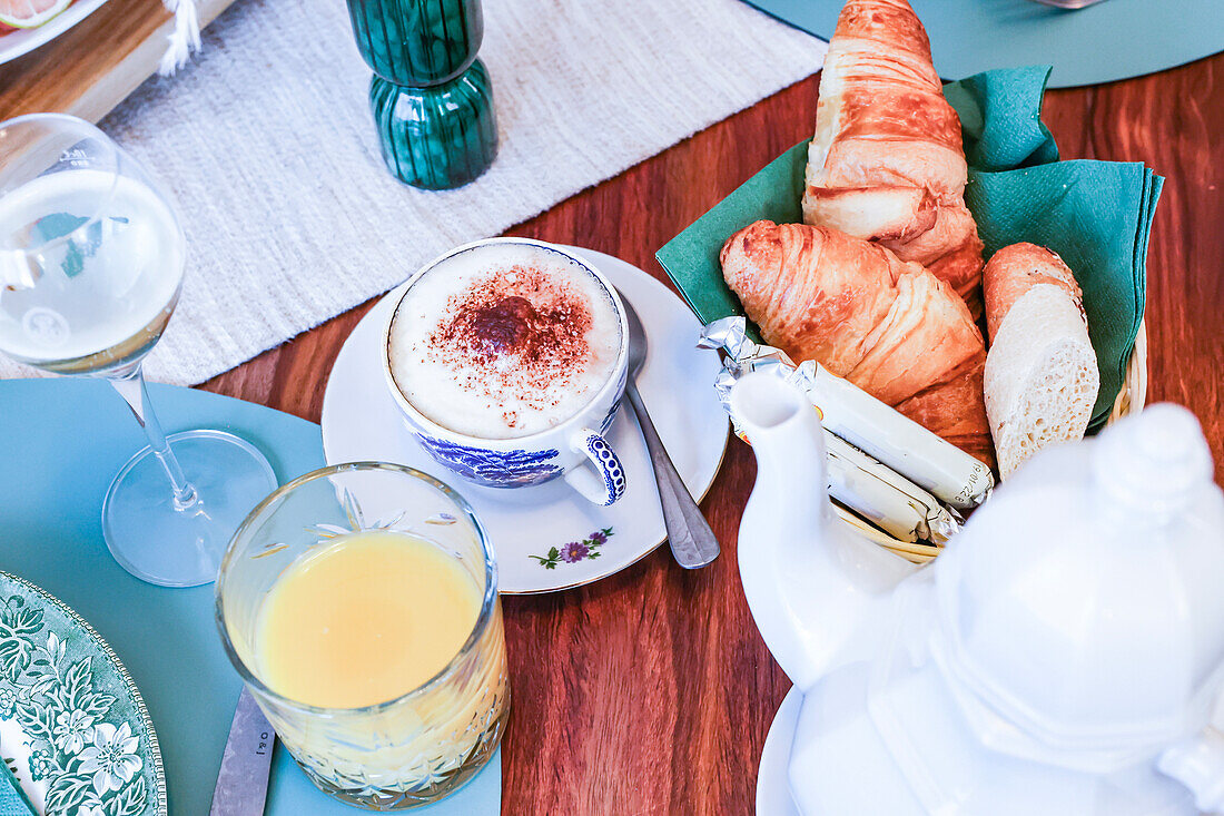 A sophisticated brunch table featuring a cappuccino, croissants, bread, and orange juice with a soothing background.