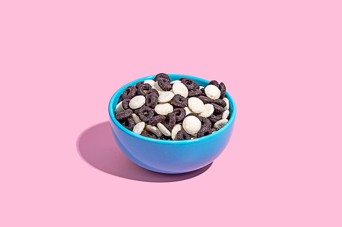 A blue bowl filled with a variety of chocolate candies captured against a soft pink background, perfect for confectionery themes.
