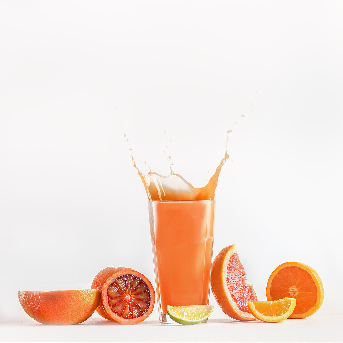 Splashing of citrus juice in glass with blood orange, grapefruit and lime at white background. Refreshing healthy drink with vitamins. Liquid in motion. Front view.